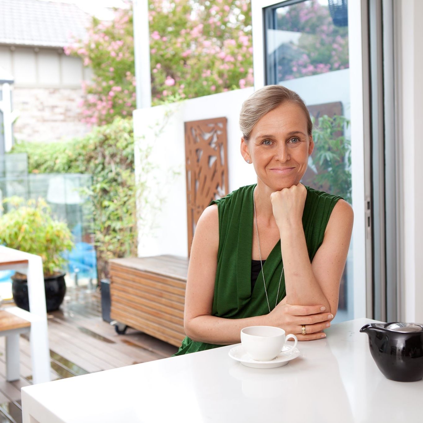 Jules seated with a cup of tea, wearing a green dress